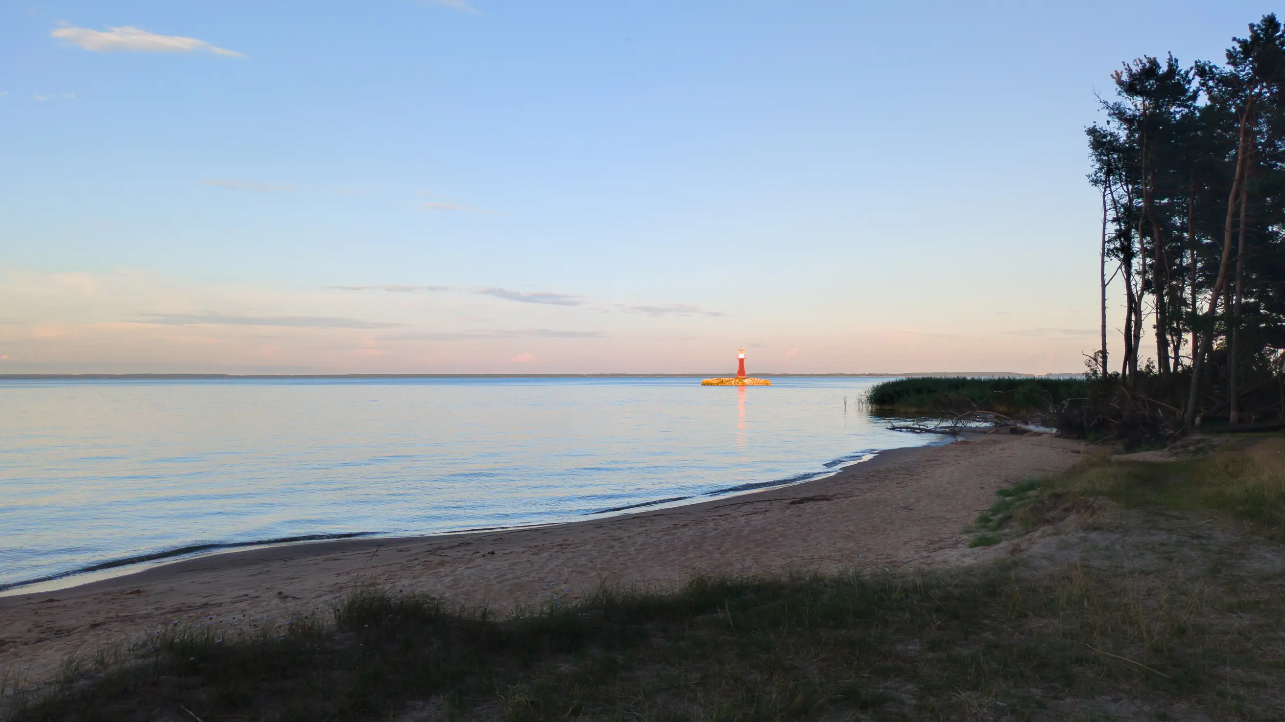 Dusk on the Curonian Spit at Pervalka: a red beacon on a stone islet, still water and pines along the sandy shore