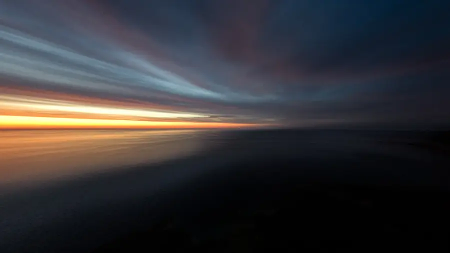 Sunset over the sea off Mallorca: a long exposure drawing the clouds into streaks, with a narrow orange band along the horizon