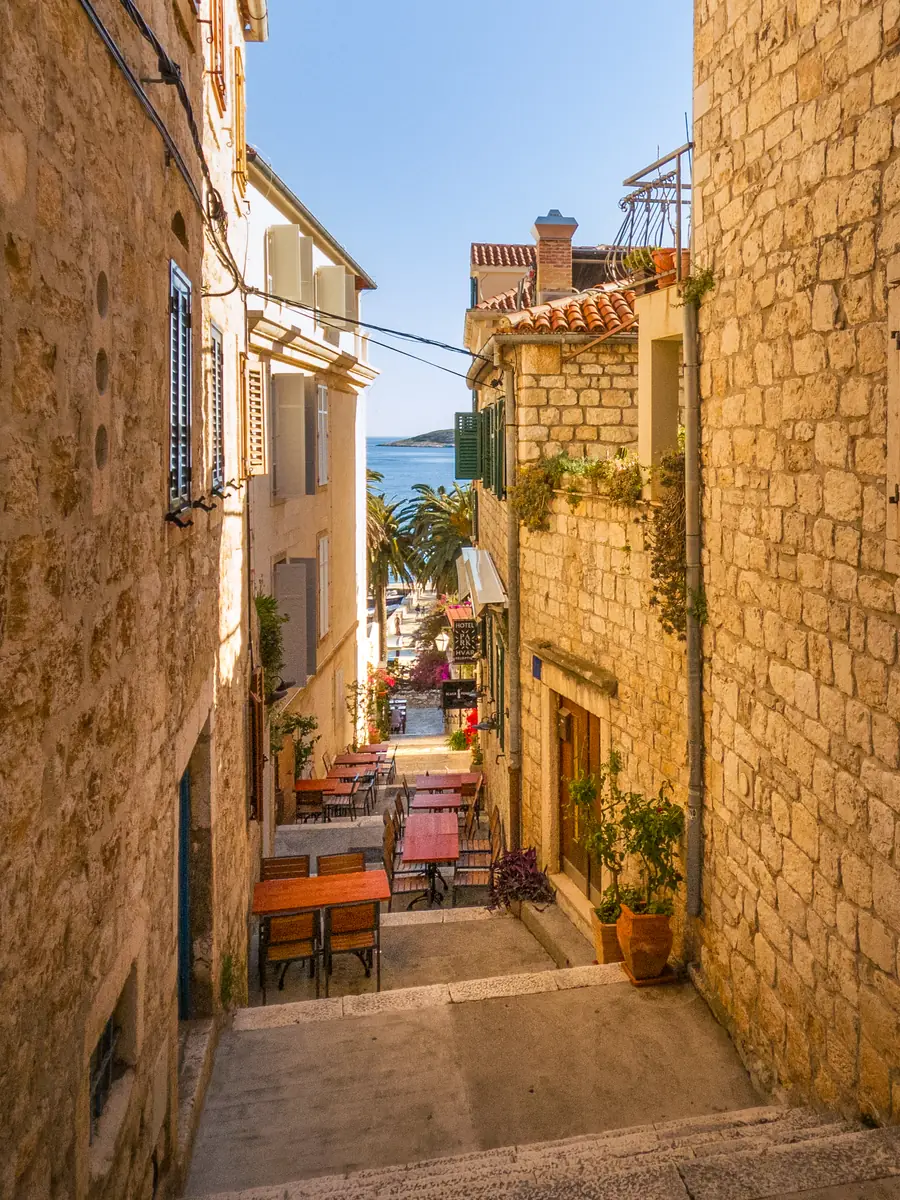 A stepped lane in Hvar town: cafe tables set out between stone walls, with palms and the sea at the bottom of the steps