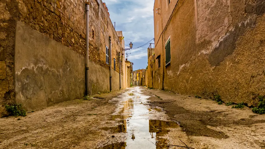 A rain-soaked alley between weathered stone walls on Mallorca, puddles running down the middle and a lamp strung overhead